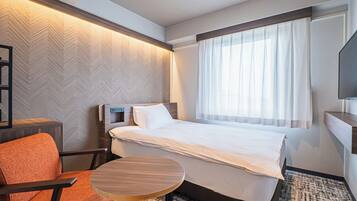 Quarto de hotel com cama, cadeira, mesa pequena, televisão e janela com cortinas.