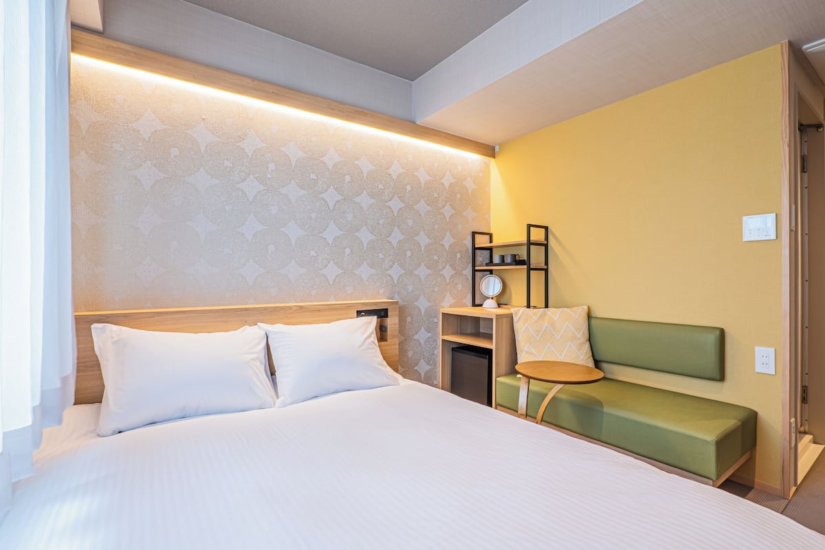 Ein Hotelzimmer mit einem Bett, einem Nachttisch, einem grünen Sofa und einem kleinen Tisch mit Lampe.