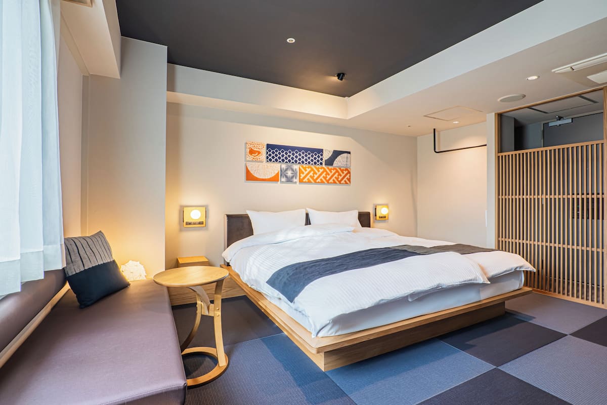 Ein modernes Hotelzimmer mit einem großen Bett, einer Sitzecke mit einer Bank und einem kleinen Tisch sowie einer Wanddekoration über dem Bett.
