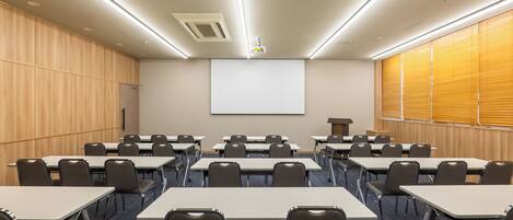 A conference room with rows of tables and chairs, a projector screen, and a podium.