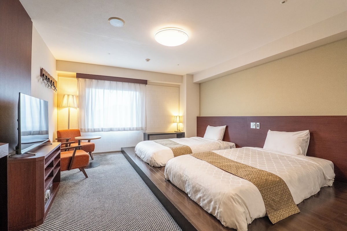Ein Hotelzimmer mit zwei Betten, einem Fernseher, einem Schreibtisch und einem Sessel.