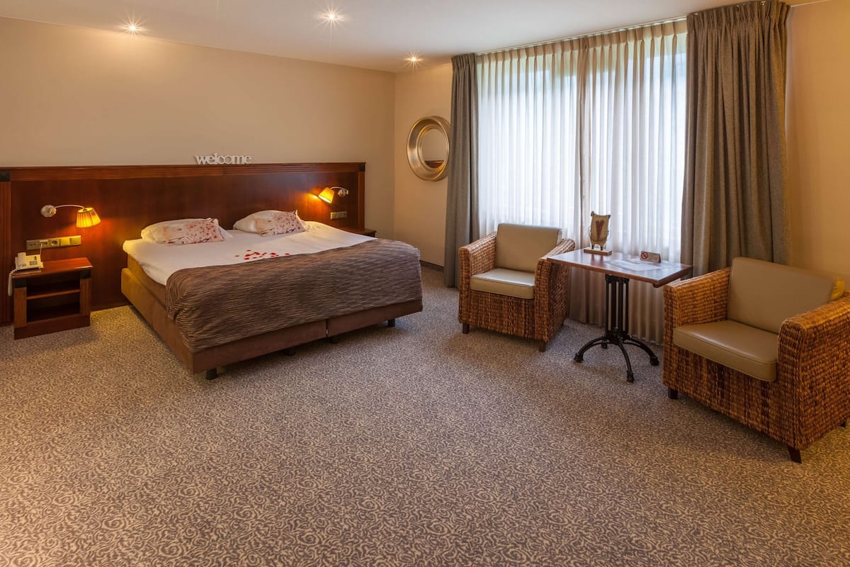 Une chambre d’hôtel avec un grand lit, deux chaises, une petite table et un miroir.