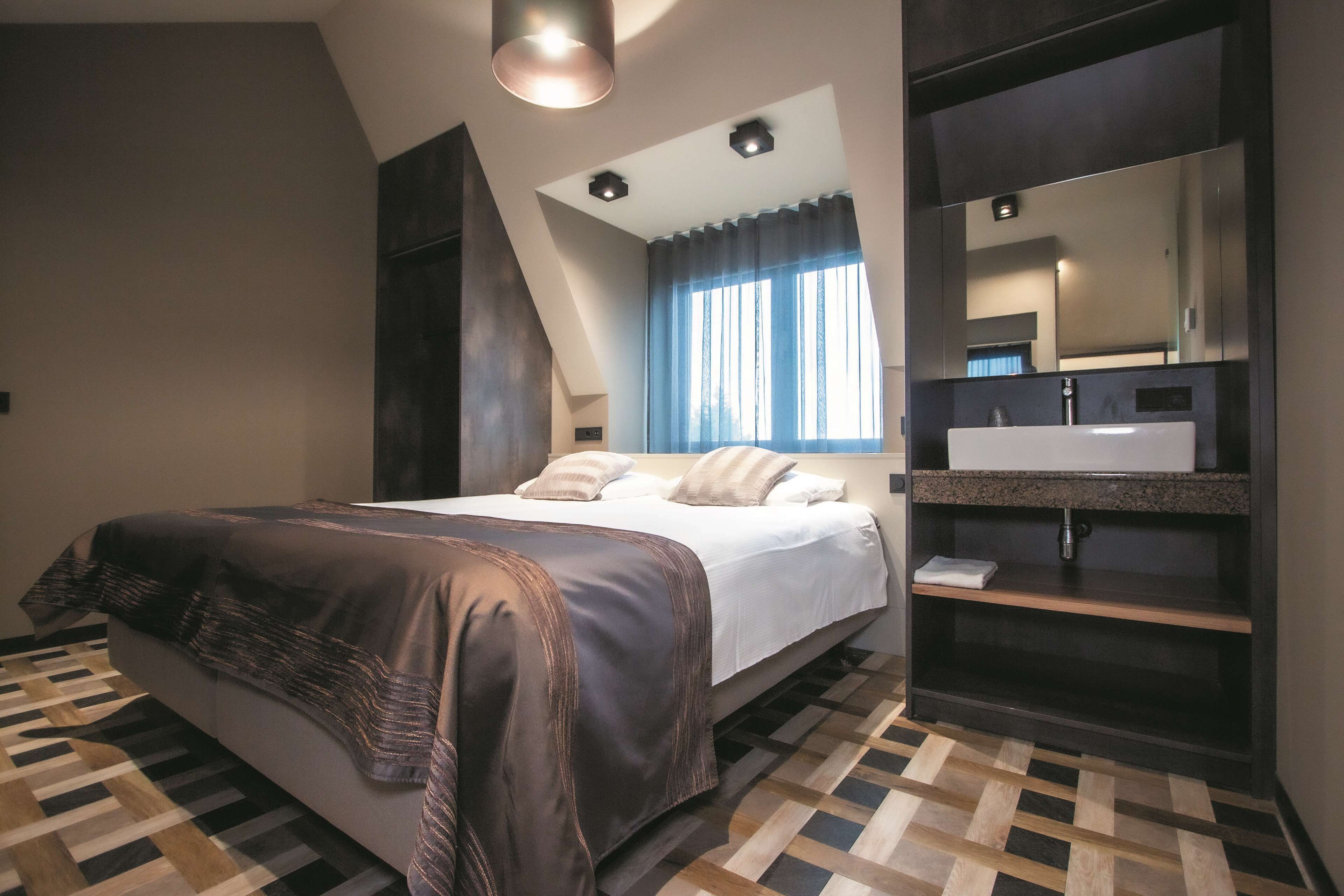 A modern bedroom with a bed, a large mirror, and a bathroom vanity.