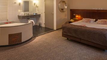 Habitación de hotel con una cama grande, baño con bañera, espejo redondo y cartel de bienvenida.