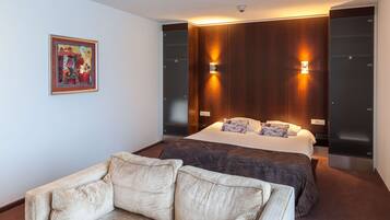 A modern hotel room with a large bed, two wall-mounted lights, a framed artwork on the wall, and a sofa.