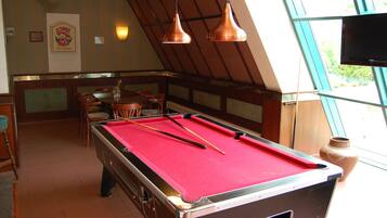 A pool table with red felt, a billiards cue, and a vase on a windowsill.