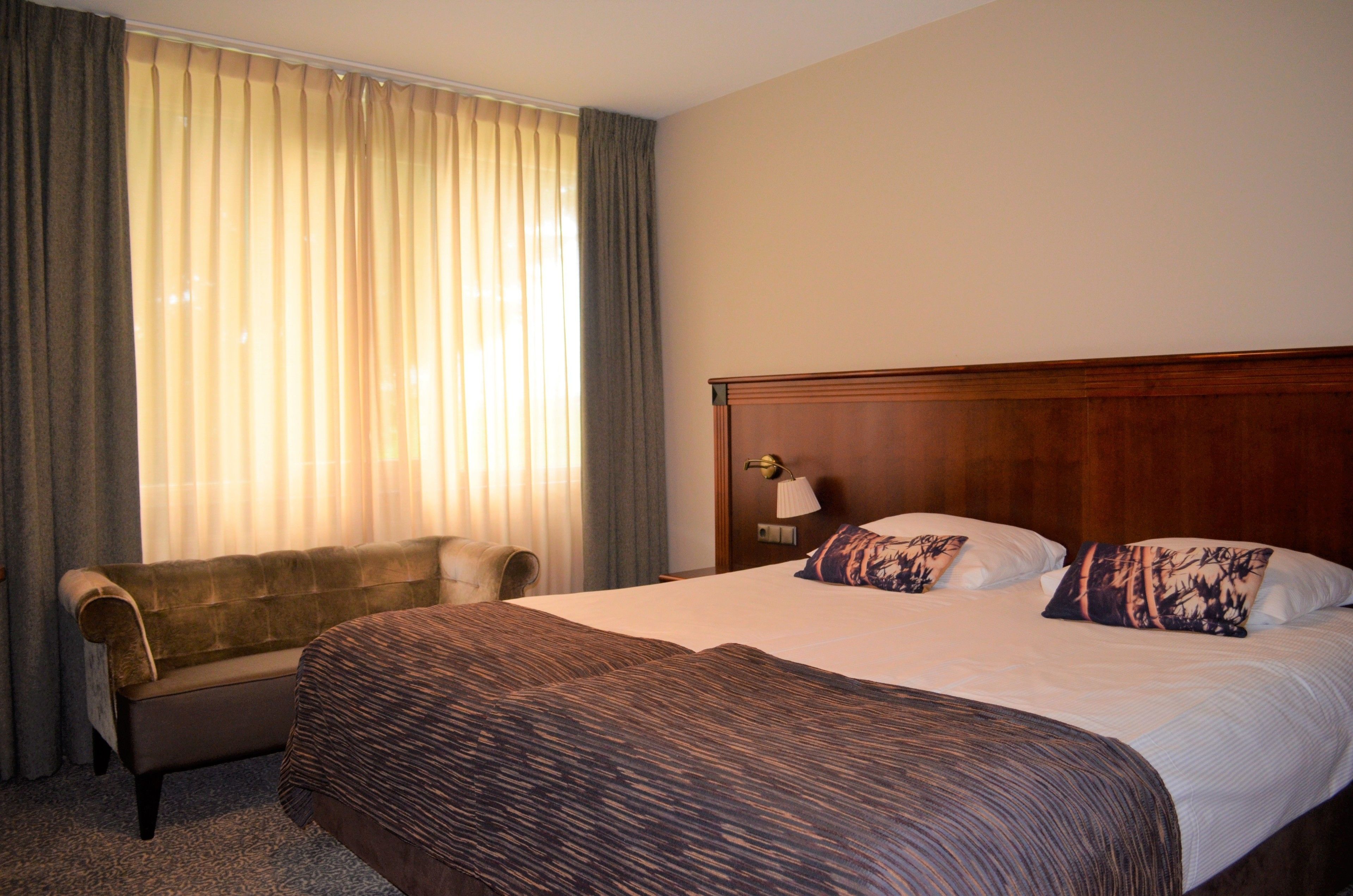 Una habitación de hotel con una cama grande, un cabecero de madera, un sofá y una ventana con cortinas.