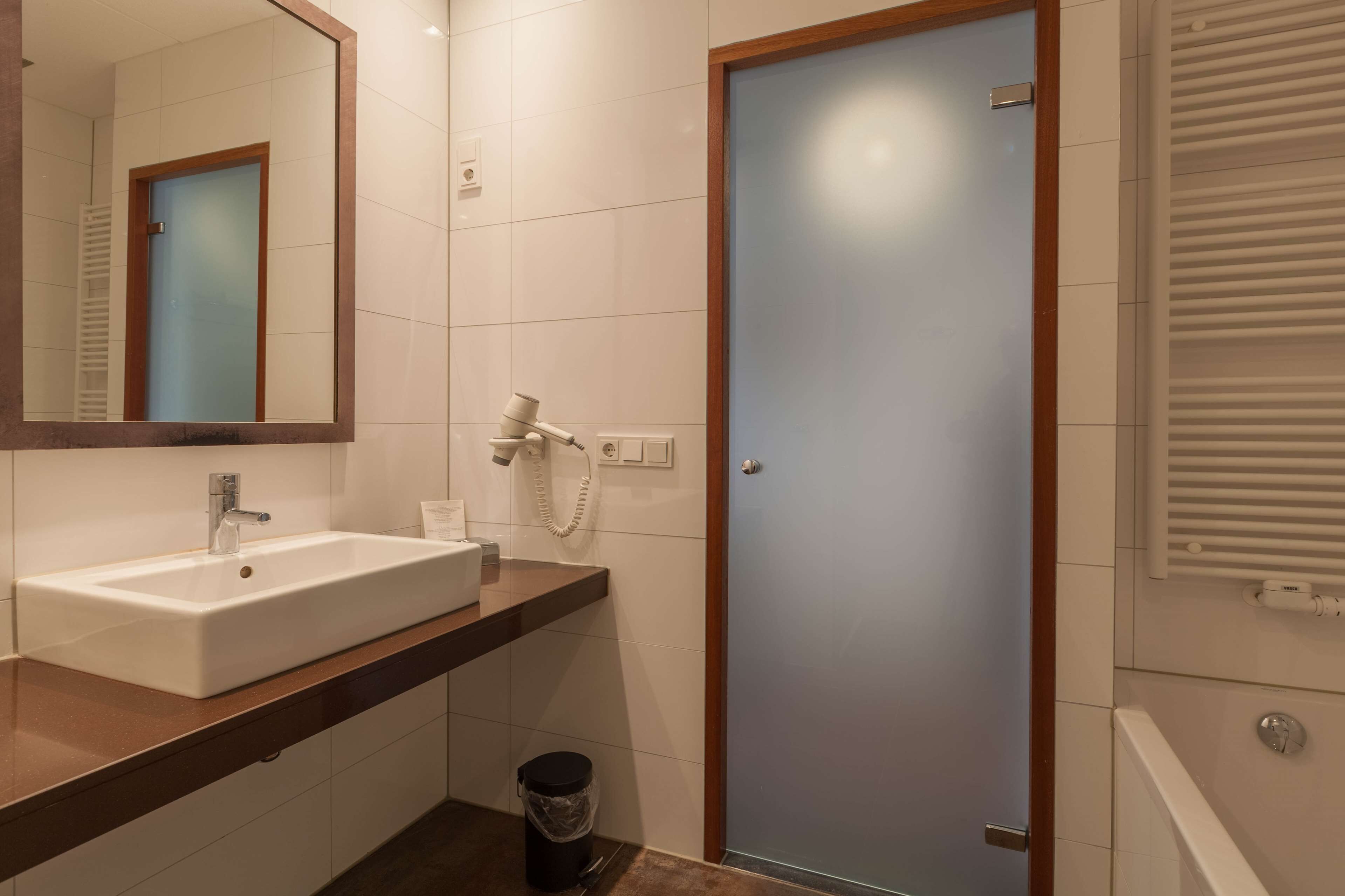 Un baño con un lavamanos blanco, un espejo, un perchero para toallas, una puerta y un radiador.