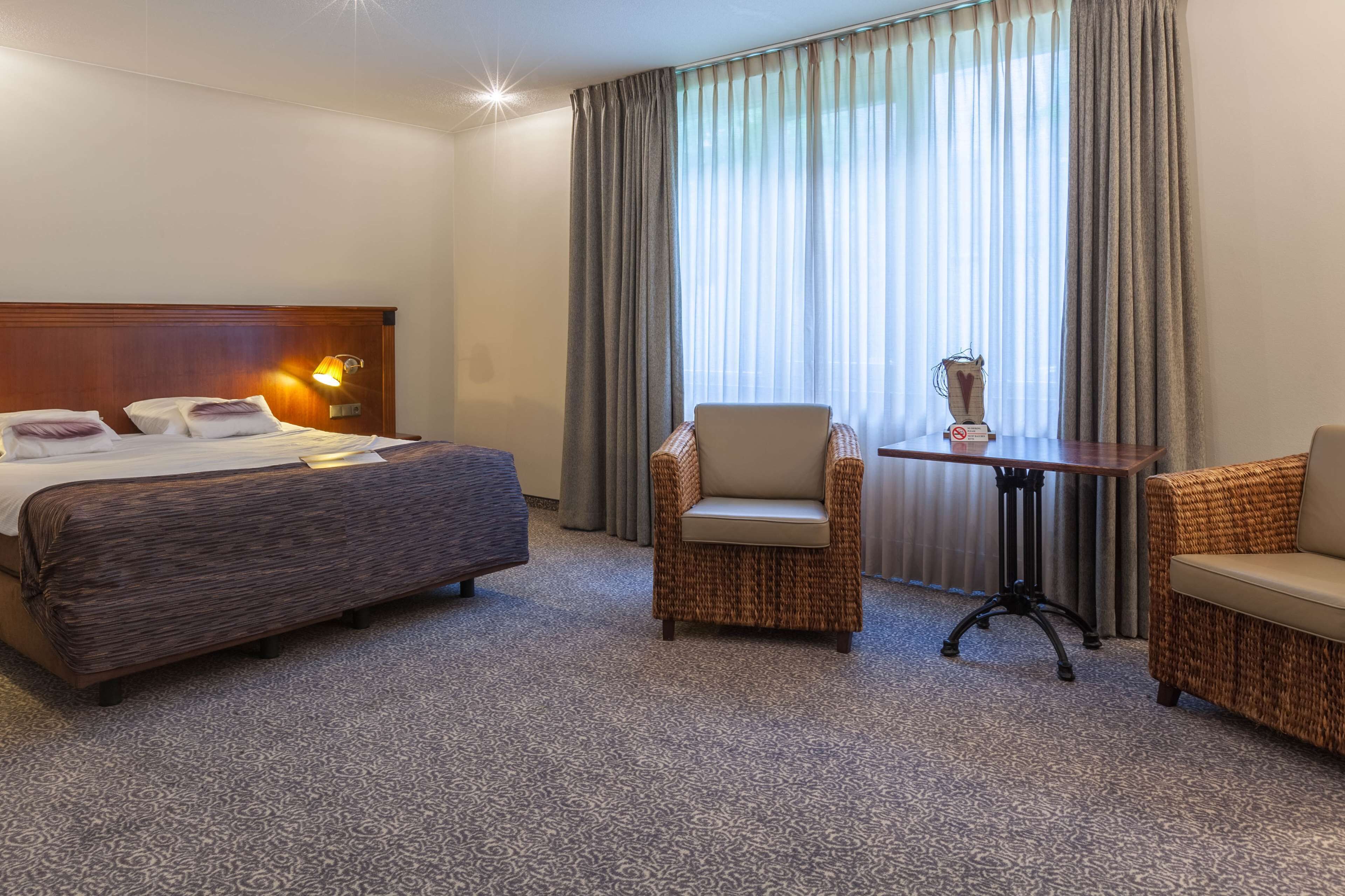 A hotel room with a large bed, two armchairs, a small table, and a lamp.