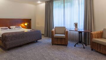 A hotel room with a large bed, two armchairs, a small table, and a lamp.