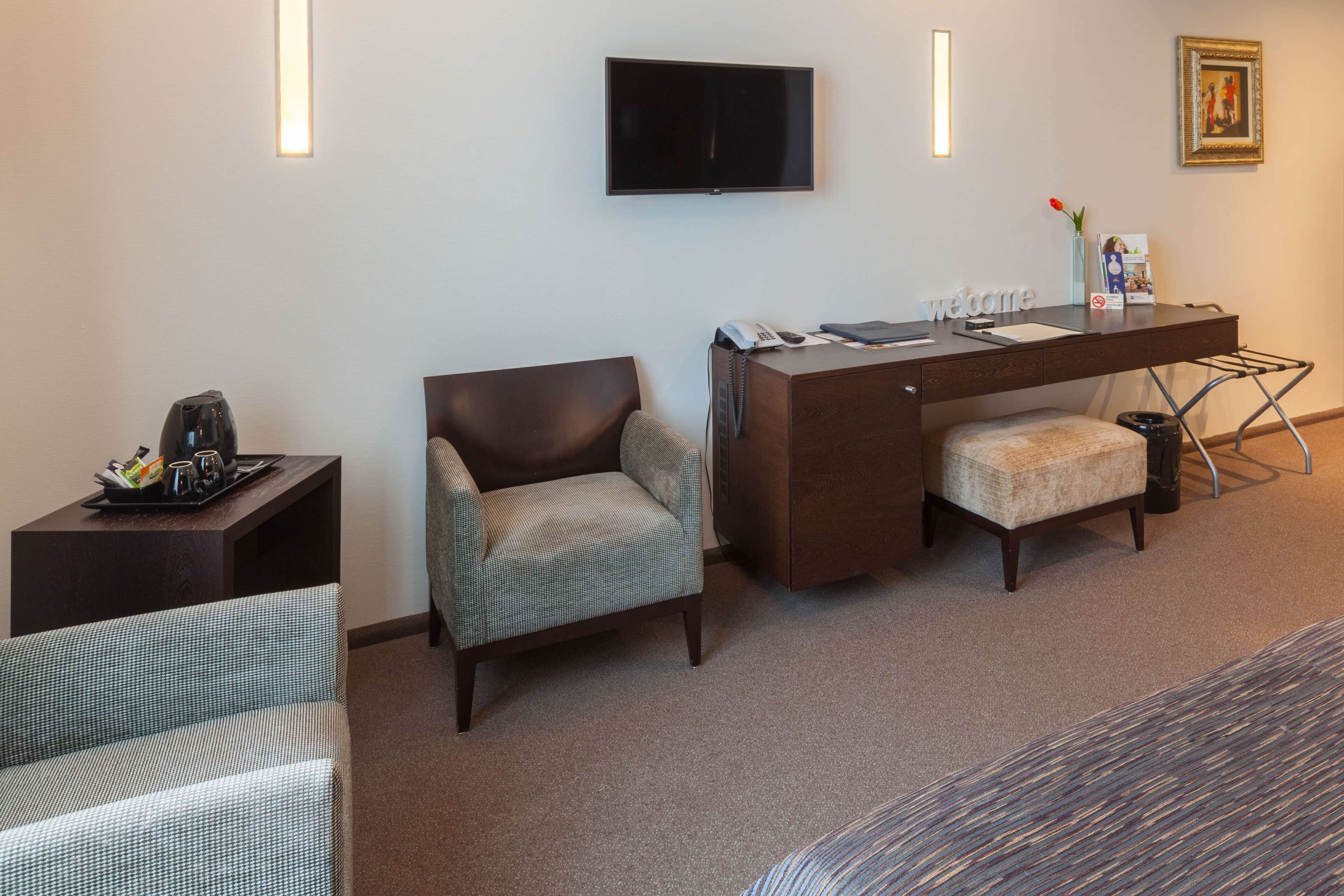 A hotel room with a bed, a desk with a chair, a television, and a small table with a tray of items.
