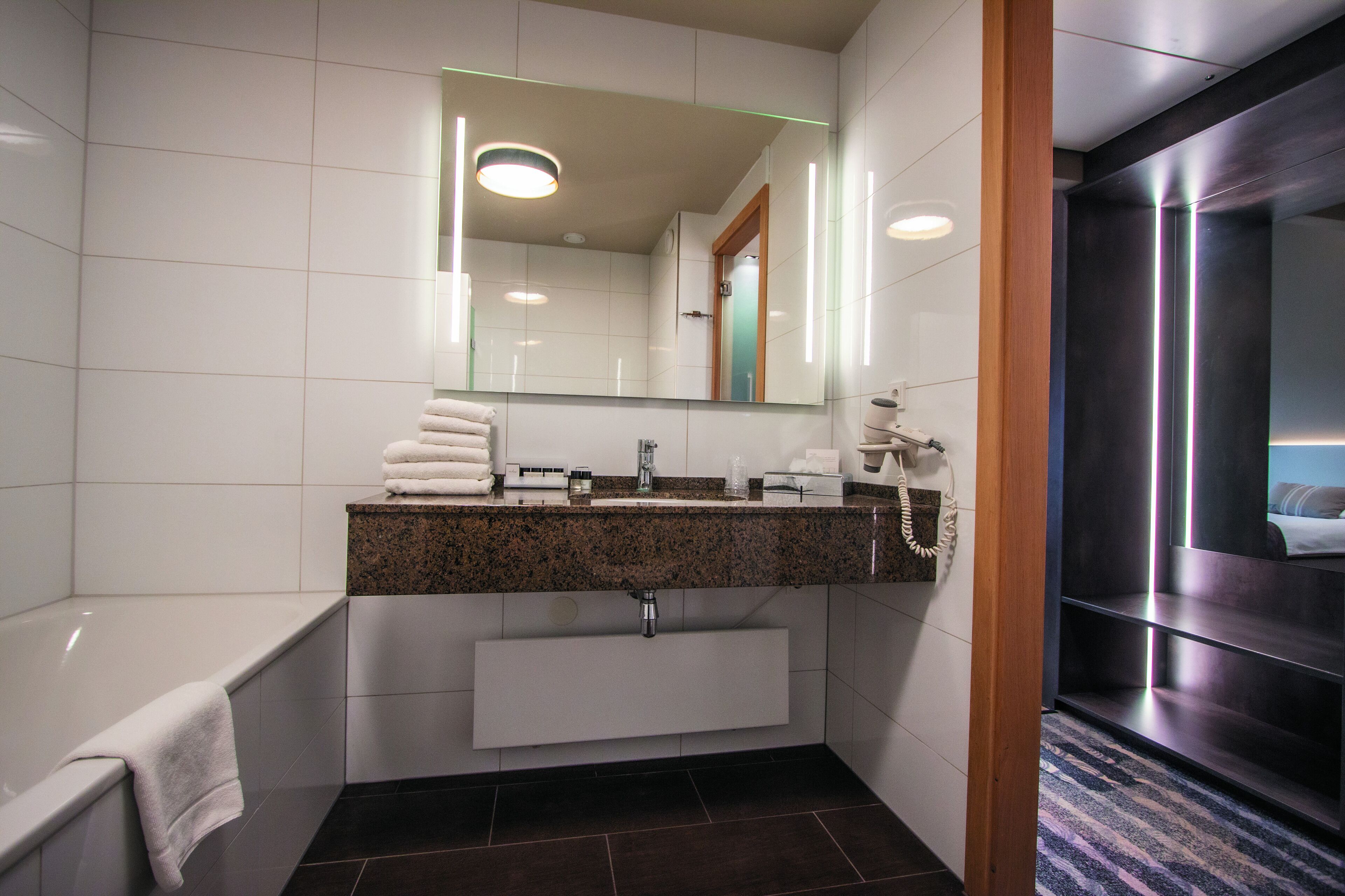 Une salle de bain moderne dotée d’un comptoir en granit, d’un grand miroir, d’un lavabo intégré et d’une baignoire séparée.