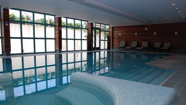 An indoor swimming pool with clear glass walls, lounge chairs, and a tiled floor. - Best Western Hotel Nobis Asten (Asten)