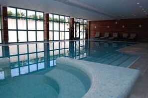 An indoor swimming pool with clear glass walls, lounge chairs, and a tiled floor. - Best Western Hotel Nobis Asten (Asten)