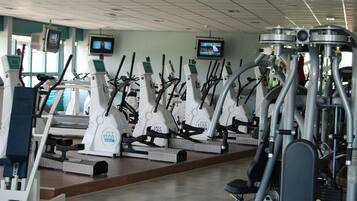 A gym with multiple cardio machines, including treadmills and elliptical trainers, arranged in rows.
