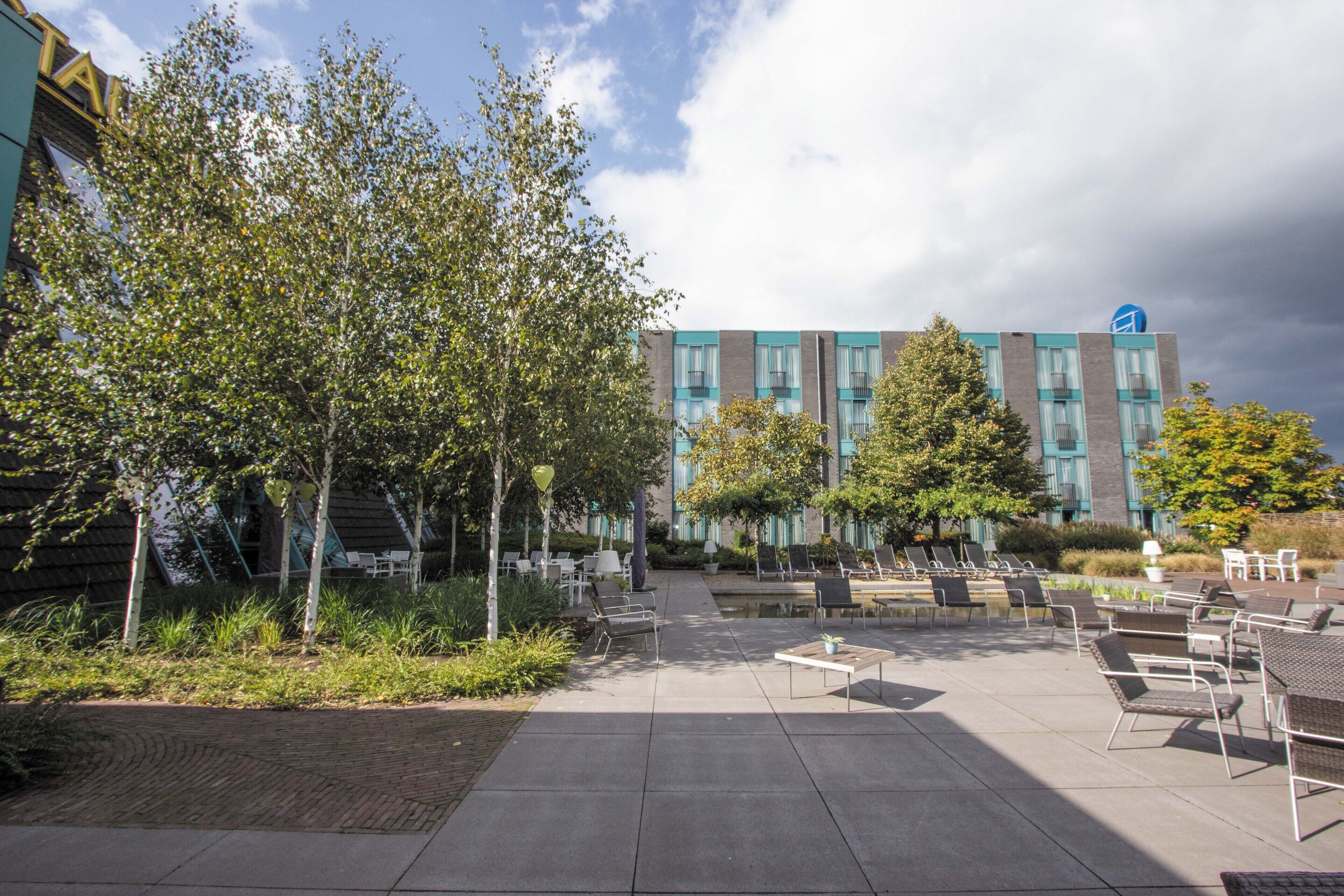 An outdoor seating area with chairs and tables, surrounded by trees and a building with large windows.