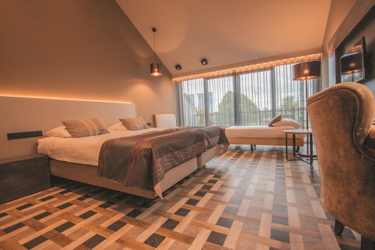 Une chambre d’hôtel moderne, dotée d’un grand lit, d’un canapé, d’un fauteuil et d’une grande fenêtre avec des rideaux.