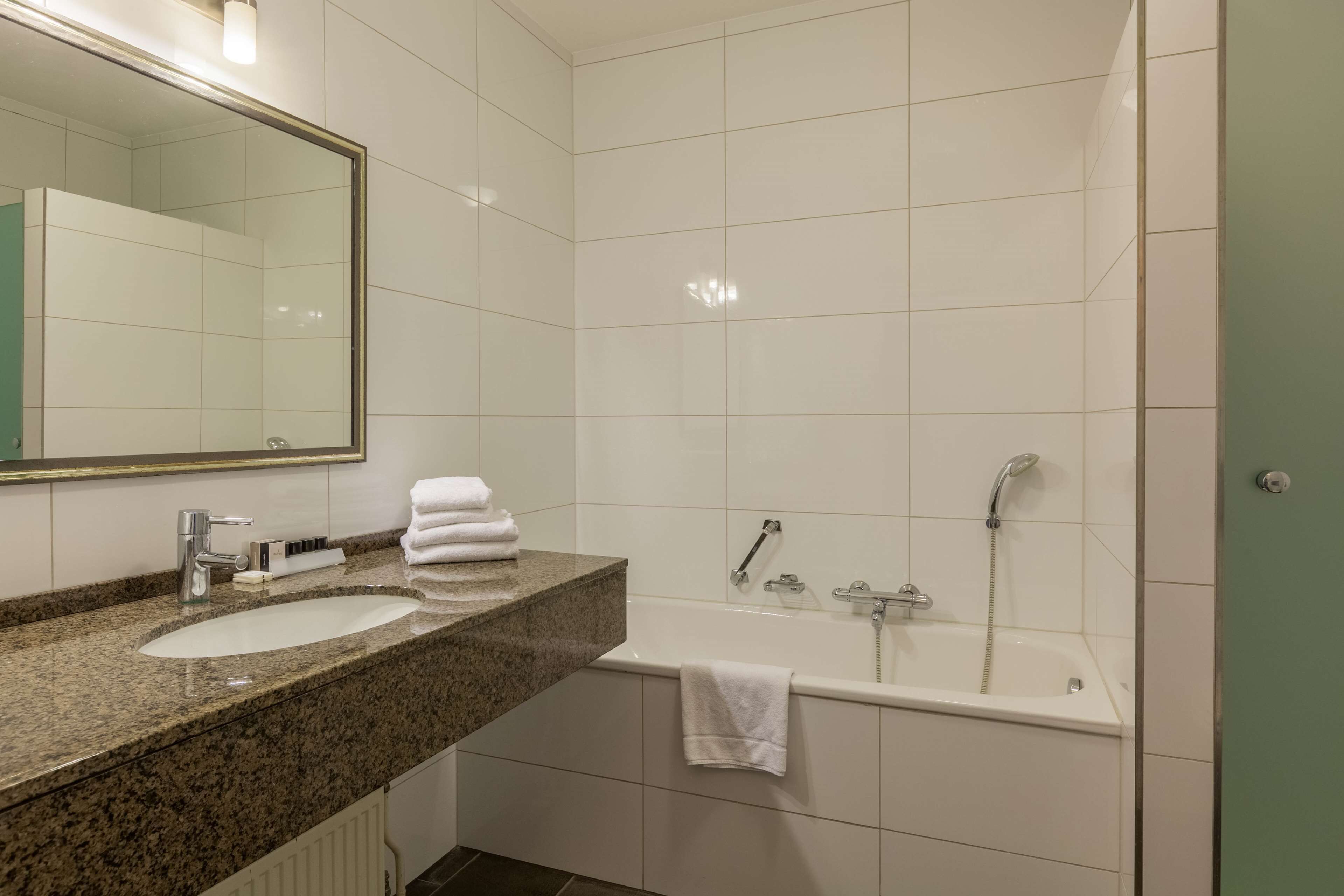 A modern bathroom with a granite countertop, two sinks, a large mirror, a bathtub, and a shower.