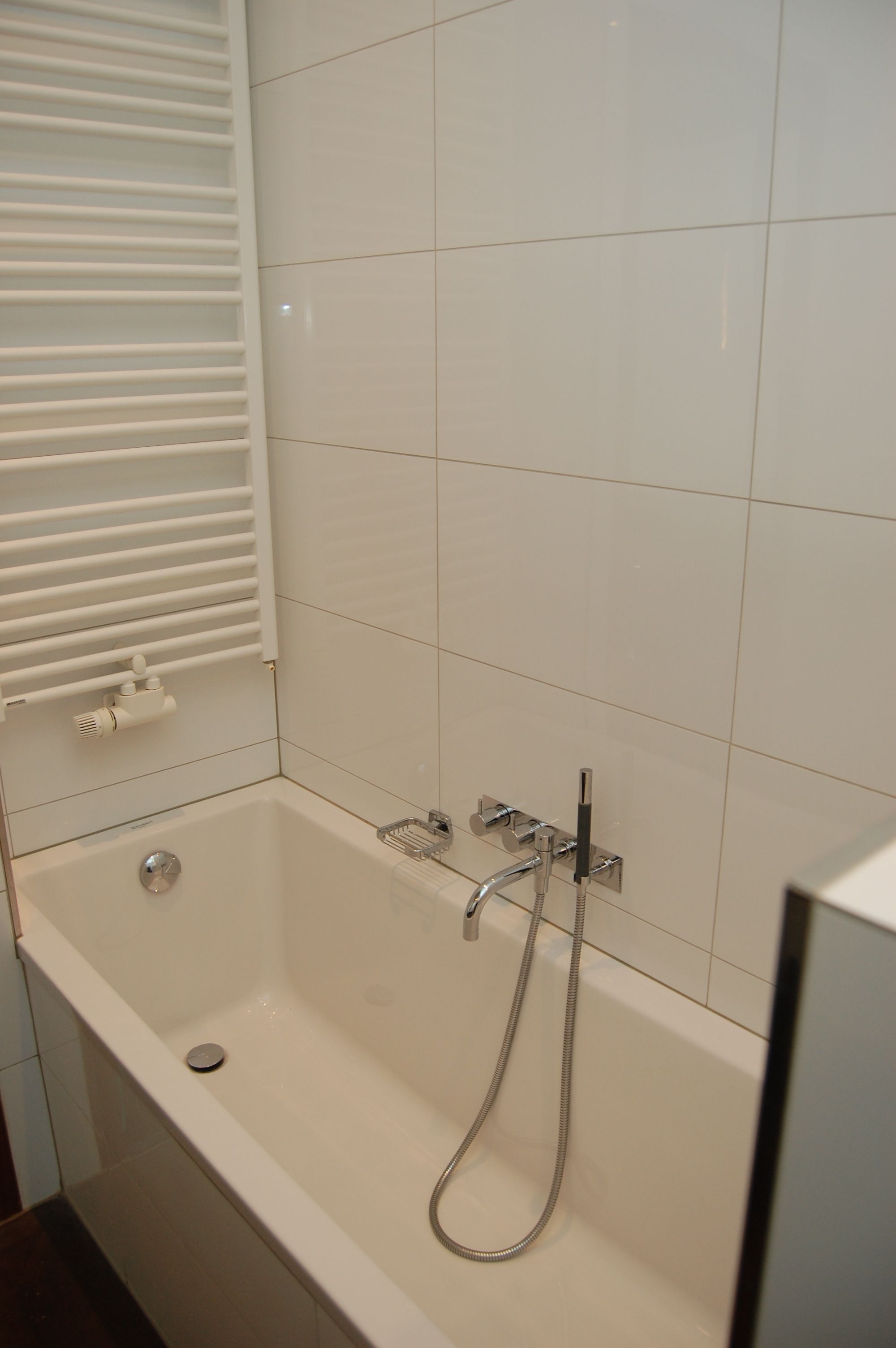A bathroom with a bathtub, a handheld showerhead, and a towel rack.