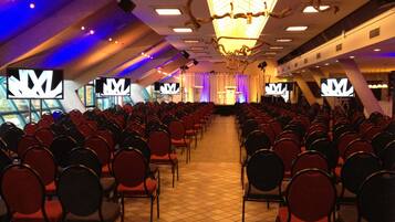 A conference room with rows of chairs, a stage with a podium, and large screens displaying a logo.