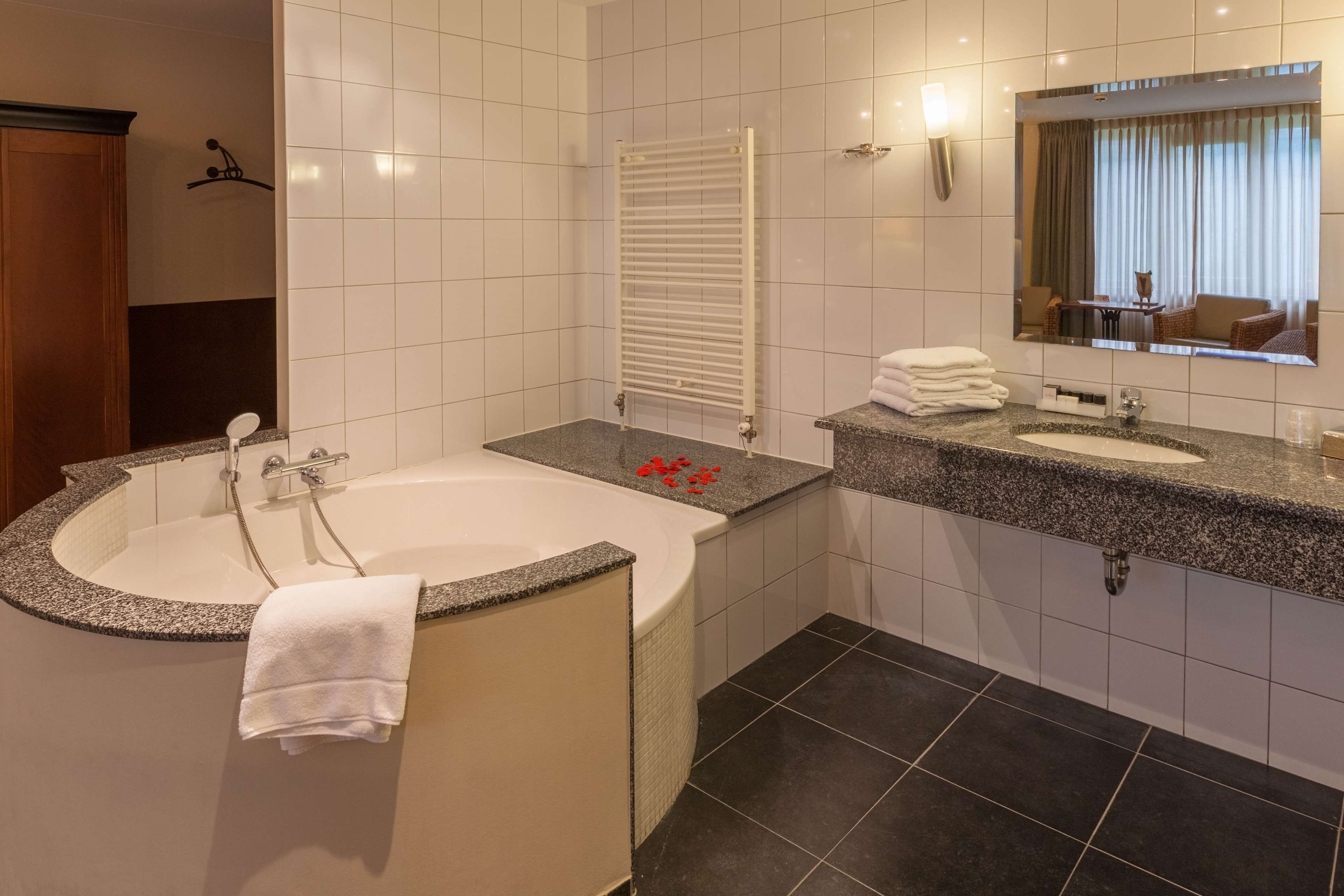 Une salle de bain moderne avec une baignoire sur pieds, un meuble-lavabo doté d’un plan de travail en granit, un grand miroir et un porte-serviettes.