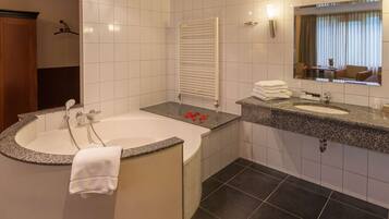 Une salle de bain moderne avec une baignoire sur pieds, un meuble-lavabo doté d’un plan de travail en granit, un grand miroir et un porte-serviettes.