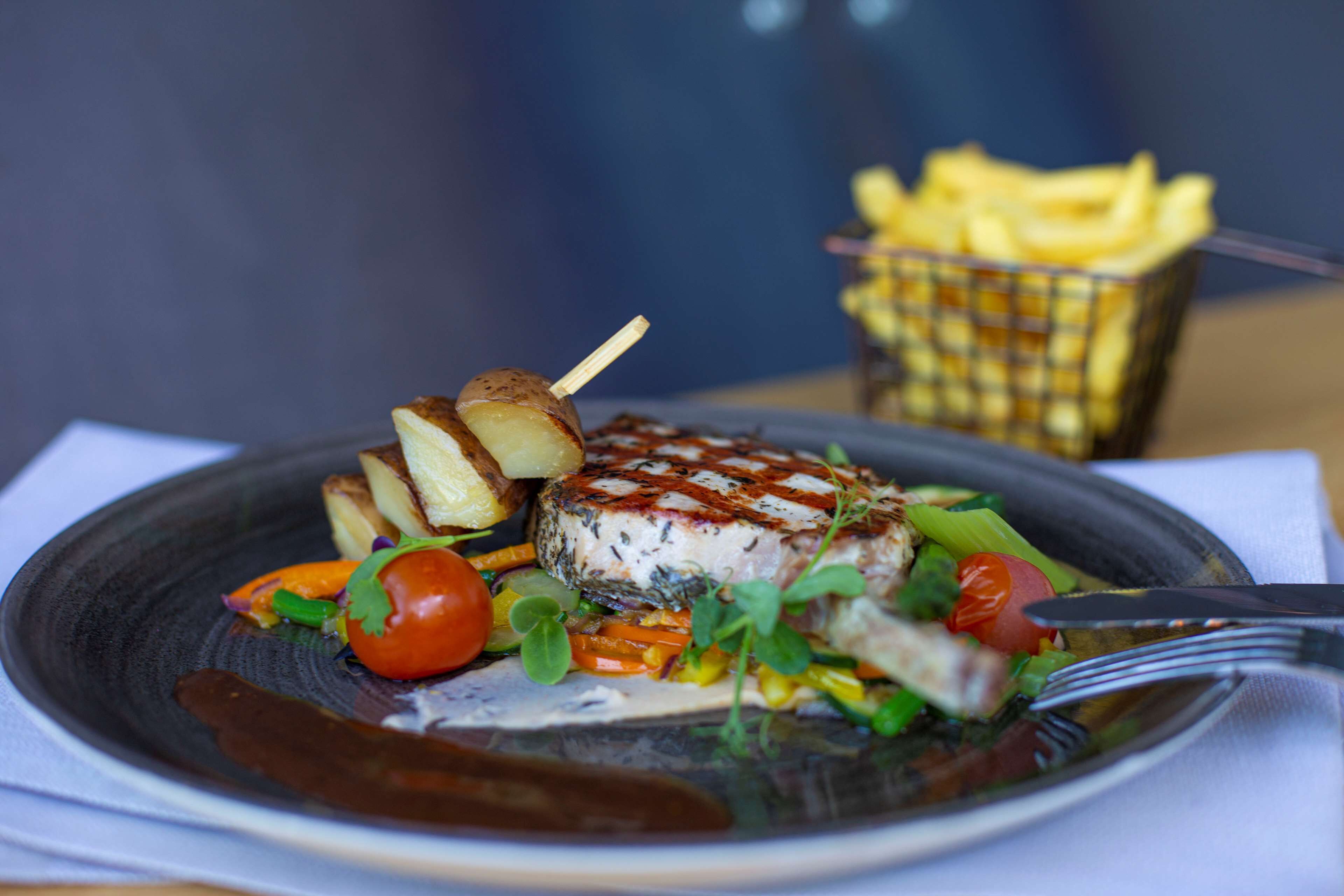 A plate of food with a grilled item, vegetables, and a side of fries.