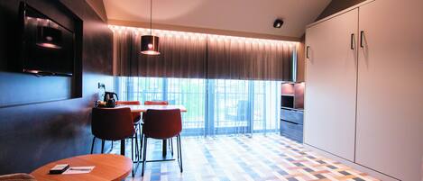 Una cocina moderna con suelo de espiga, un comedor con mesa y sillas redondas, y ventanas grandes con cortinas ligeras.