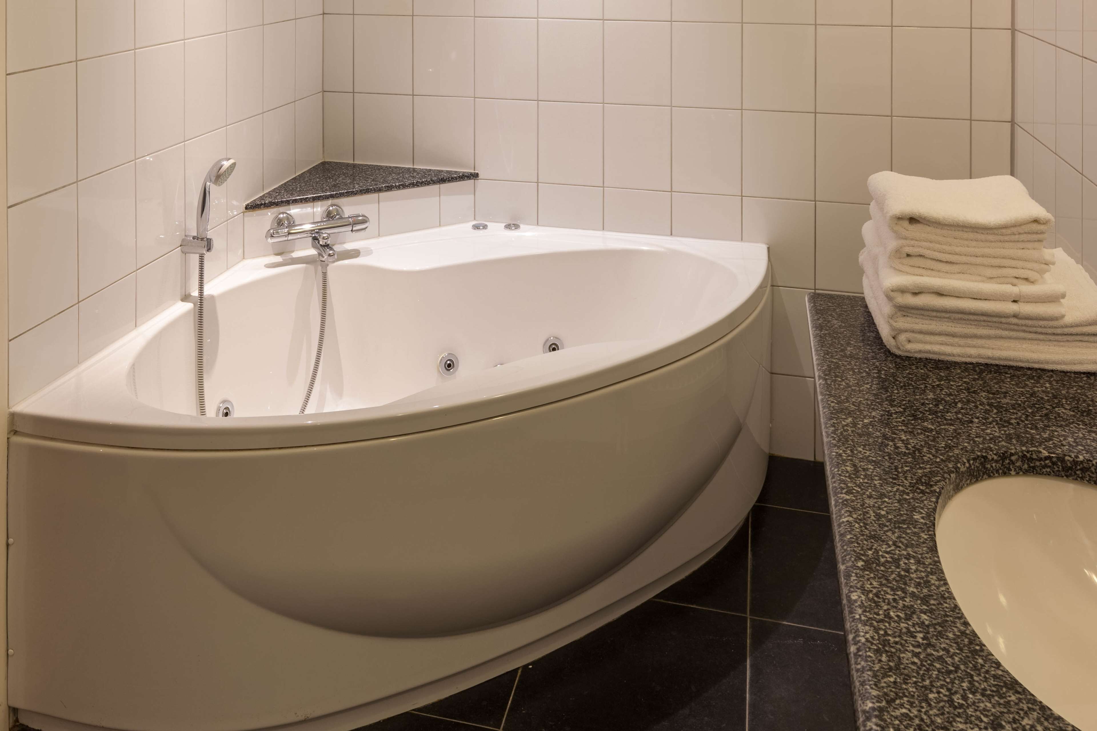 Een moderne badkamer met een vrijstaand bad, een granieten aanrechtblad en een stap handdoeken.