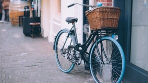 A bicycle with a basket and fenders parked against a building.