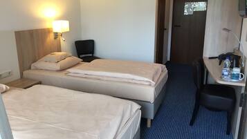 Een hotelkamer met twee bedden, een bureau met stoel, een lamp en een deur.