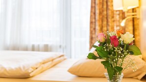 A neatly made bed with a vase of flowers on the side. - Hotel Kelkheimer Hof (Kelkheim)