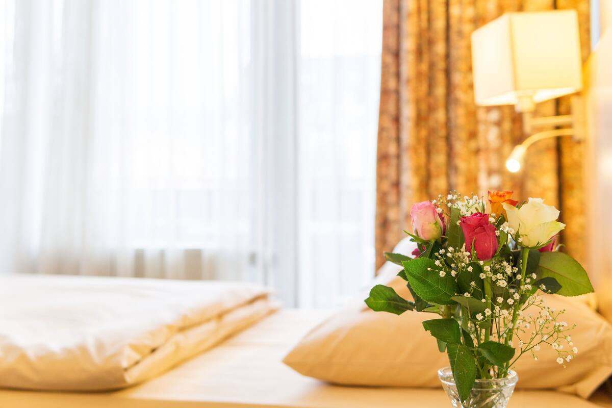 Een opgemaakt bed met een vaas bloemen ernaast.