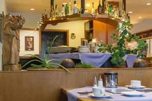 Ein Restaurantinnenraum mit einer Holzbänkl, einer Statue, einem Topfpflanze und einer Bar mit Flaschen.