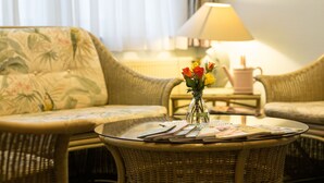 A wicker sofa with floral upholstery, a glass coffee table with magazines, and a vase with flowers. - Hotel Kelkheimer Hof (Kelkheim)