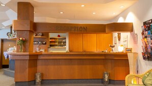 A reception area with a wooden reception desk, a wall-mounted bulletin board, and a wicker sofa. - Hotel Kelkheimer Hof (Kelkheim)