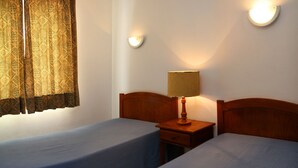 A room with two single beds, a nightstand with a lamp, and a wall-mounted light fixture. - Apartamentos Kings (Loule)