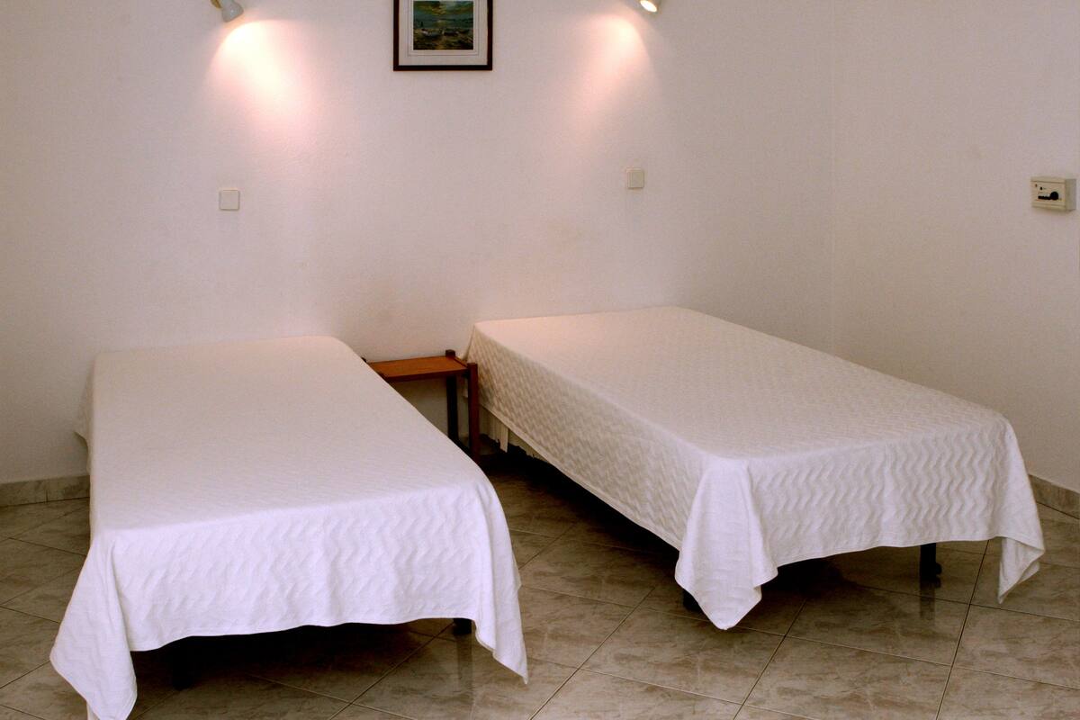 Two single beds with white linens in a room with white walls and tiled flooring.