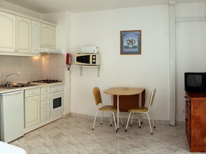 A compact kitchen with a stove, sink, and microwave. There is a small dining table with two chairs. A framed picture hangs on the wall. - Apartamentos Kings (Loule)