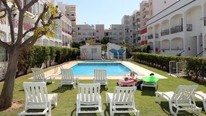 A swimming pool with white lounge chairs and a small building in the center. - Apartamentos Kings (Loule)