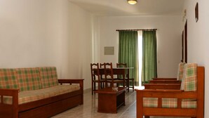 A living room with a sofa, chairs, a coffee table, and a dining table. - Apartamentos Kings (Loule)