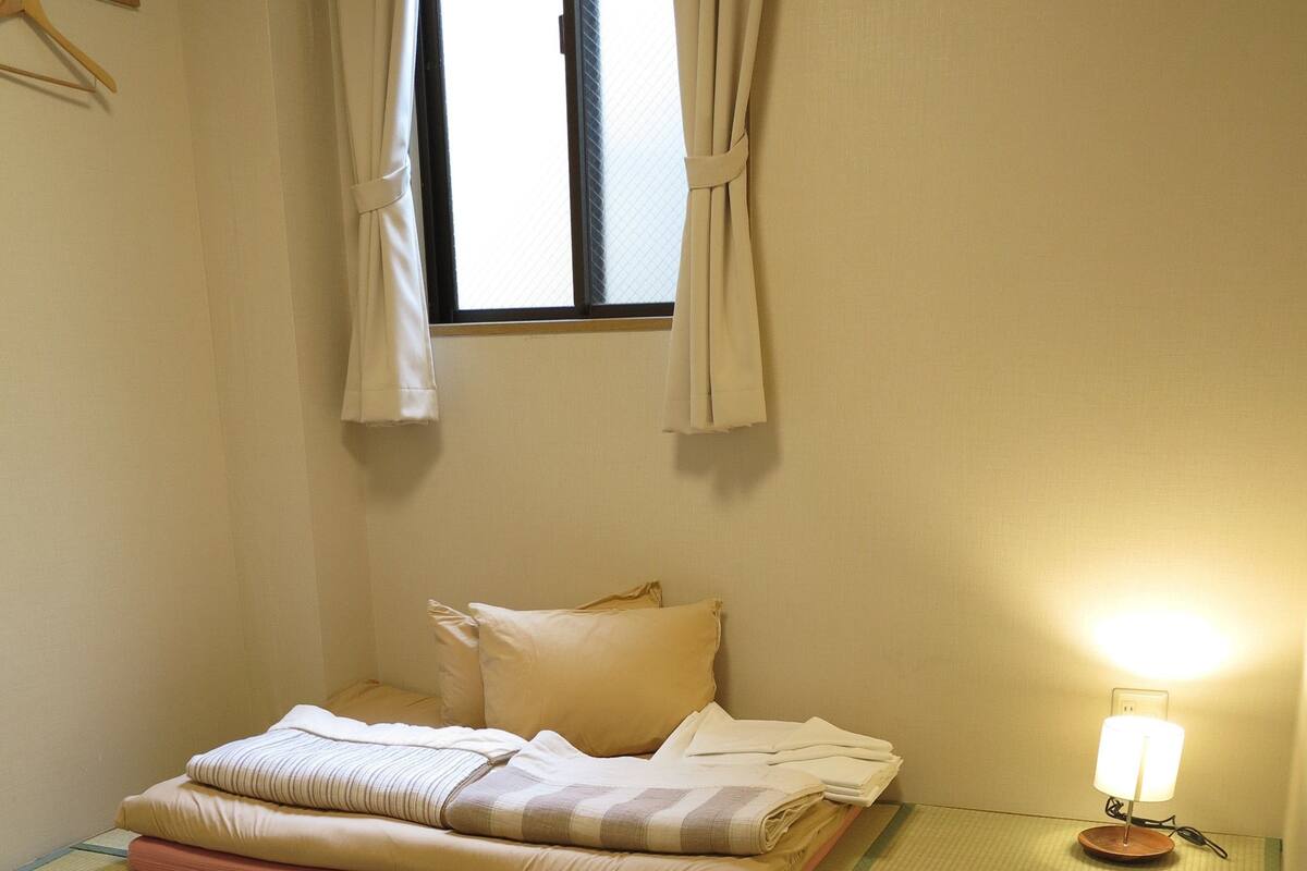 Ein traditioneller japanischer Raum mit Tatami-Böden, einem niedrigen Holztisch und einem Bett mit Kissen und Decke.