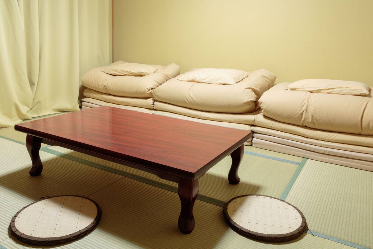 Ein traditioneller japanischer Raum mit Tatami-Böden, einem niedrigen Holztisch und einer Couch mit Kissen.