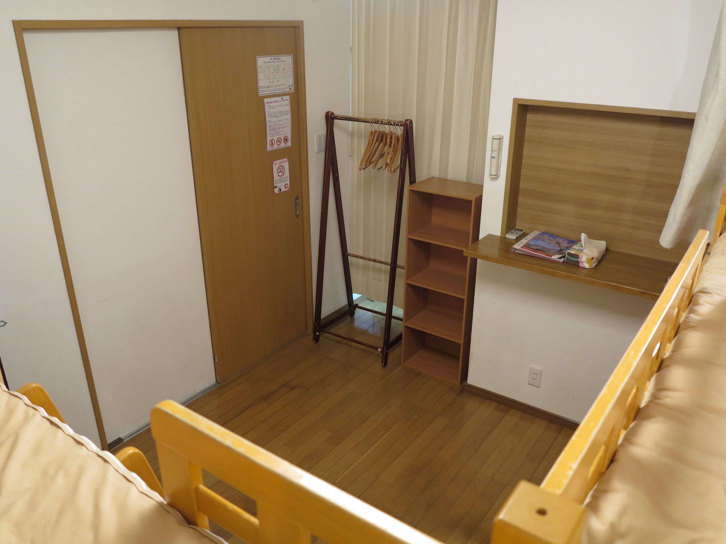 A small, compact room with a wooden bed, a wooden shelf with books, a wooden wardrobe, and a wooden ladder.