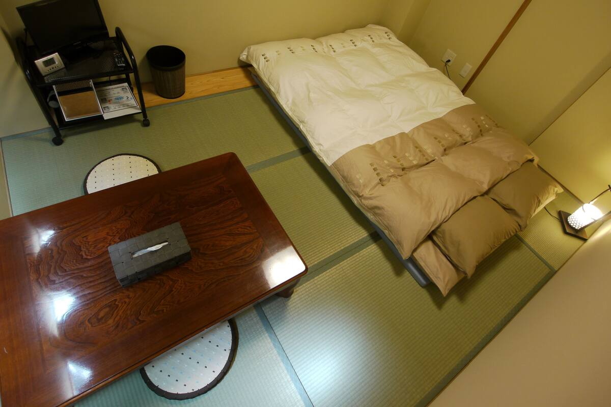 Ein Zimmer mit einem Bett, einem kleinen Tisch, einem Stuhl und einem Mülleimer.