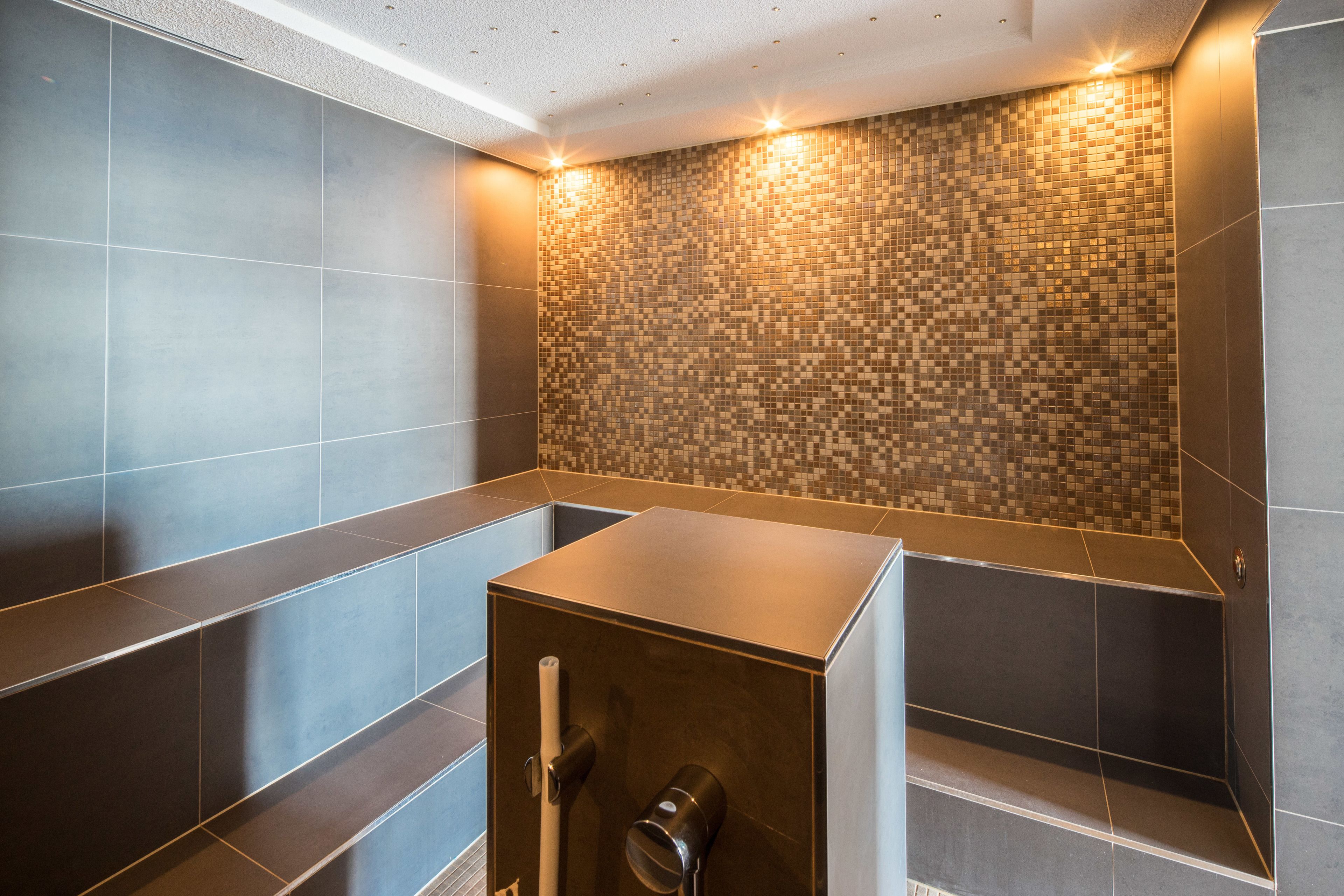 A modern bathroom with a tiled wall, a built-in shower, and a bench.