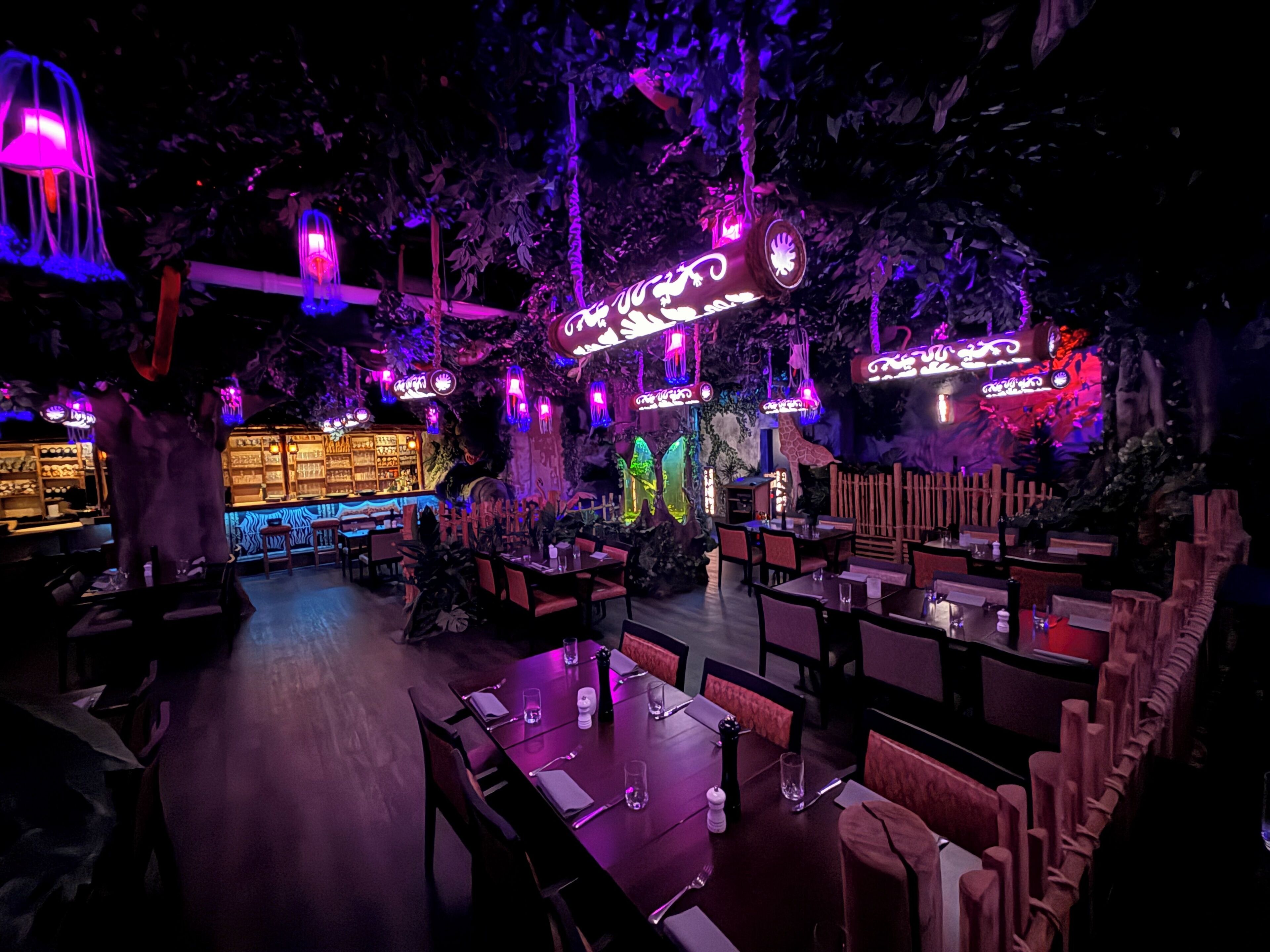 An indoor restaurant with tables and chairs, a bar area, and decorative lighting.
