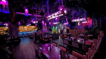 Ein Restaurant mit Tischen, Stühlen, einer Bar und dekorativer Beleuchtung.
