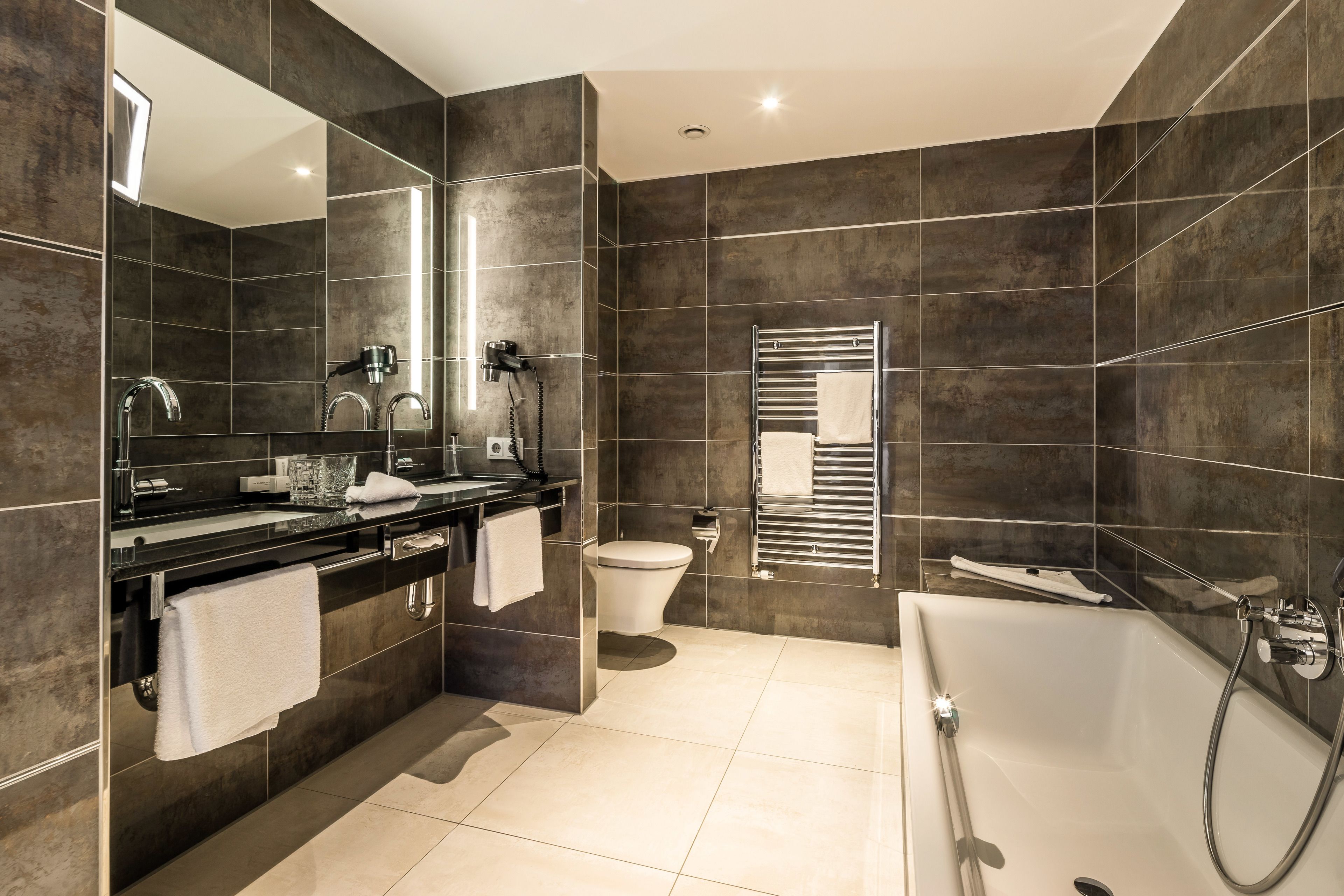 A modern bathroom with a large mirror, a black countertop, a toilet, and a bathtub.