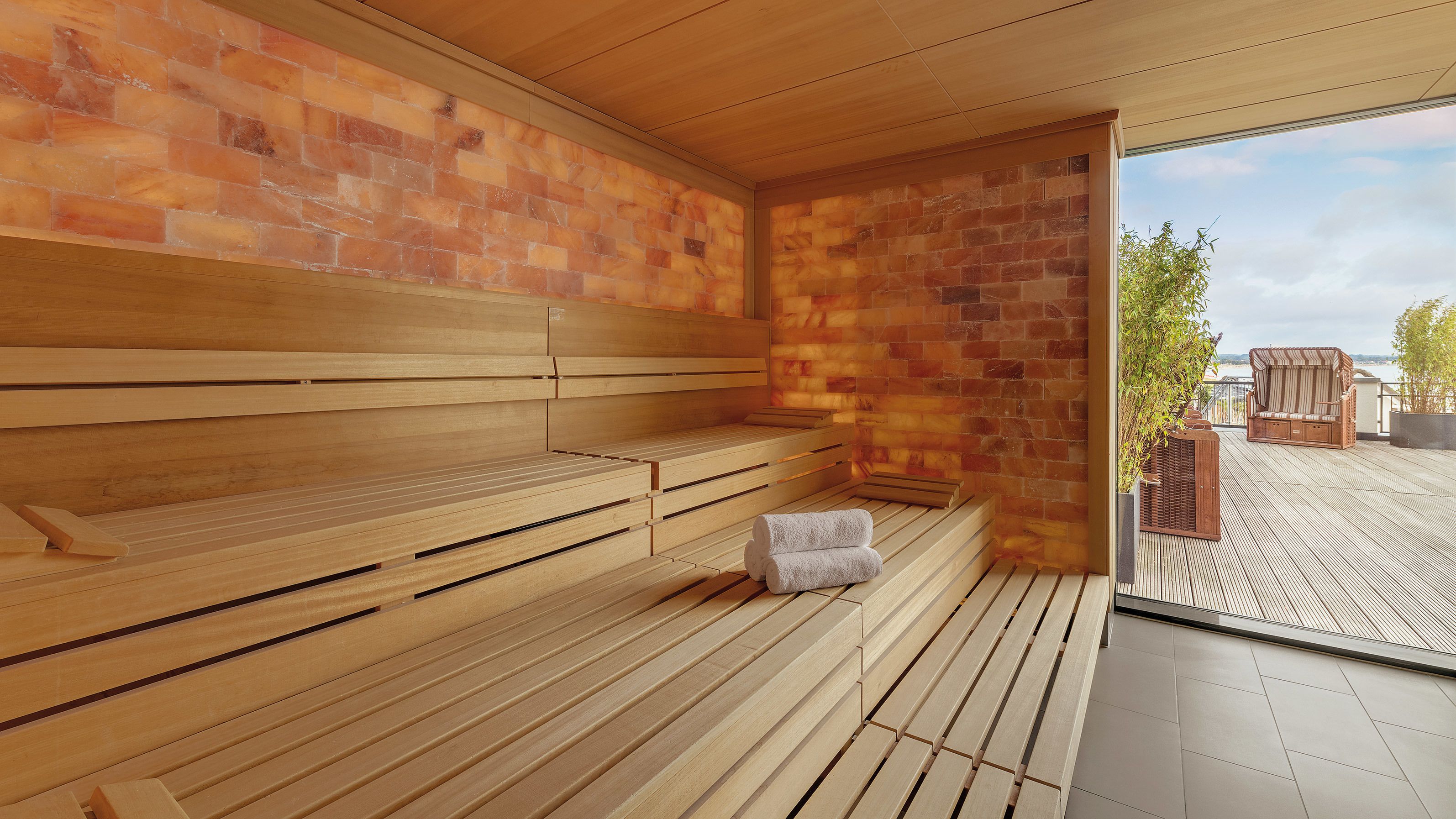 Eine Sauna mit Holzbänken und einer Ziegelwand, ein Handtuch auf dem Boden und Blick ins Freie.